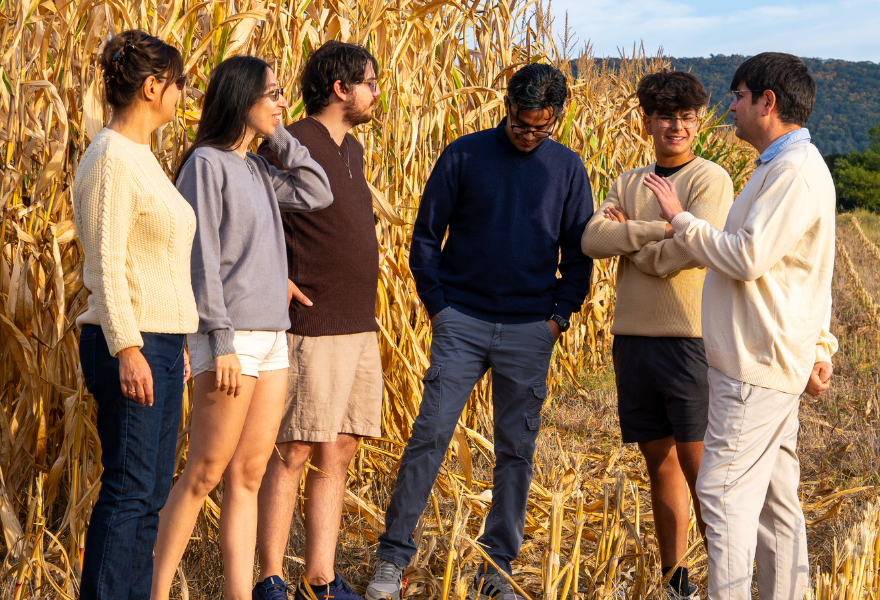  Six people standing and talking in a cornfield, with their faces obscured, wearing casual sweaters and outdoor clothing